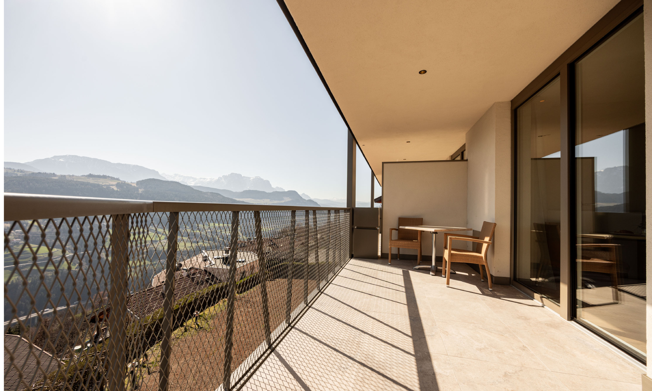 Balkon mit Tisch und Stühlen und Blick auf die Dolomiten und ins Tal - Egger Apartments & Suites