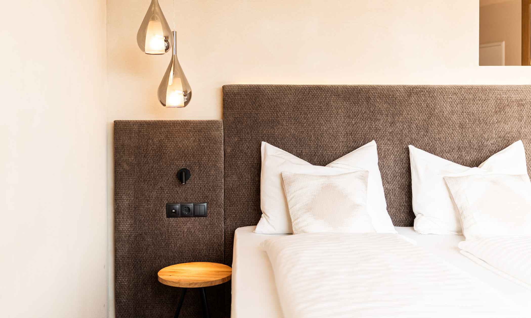 sauber gemachtes Bett mit modernen Hängelampen - Egger Apartments & Suites