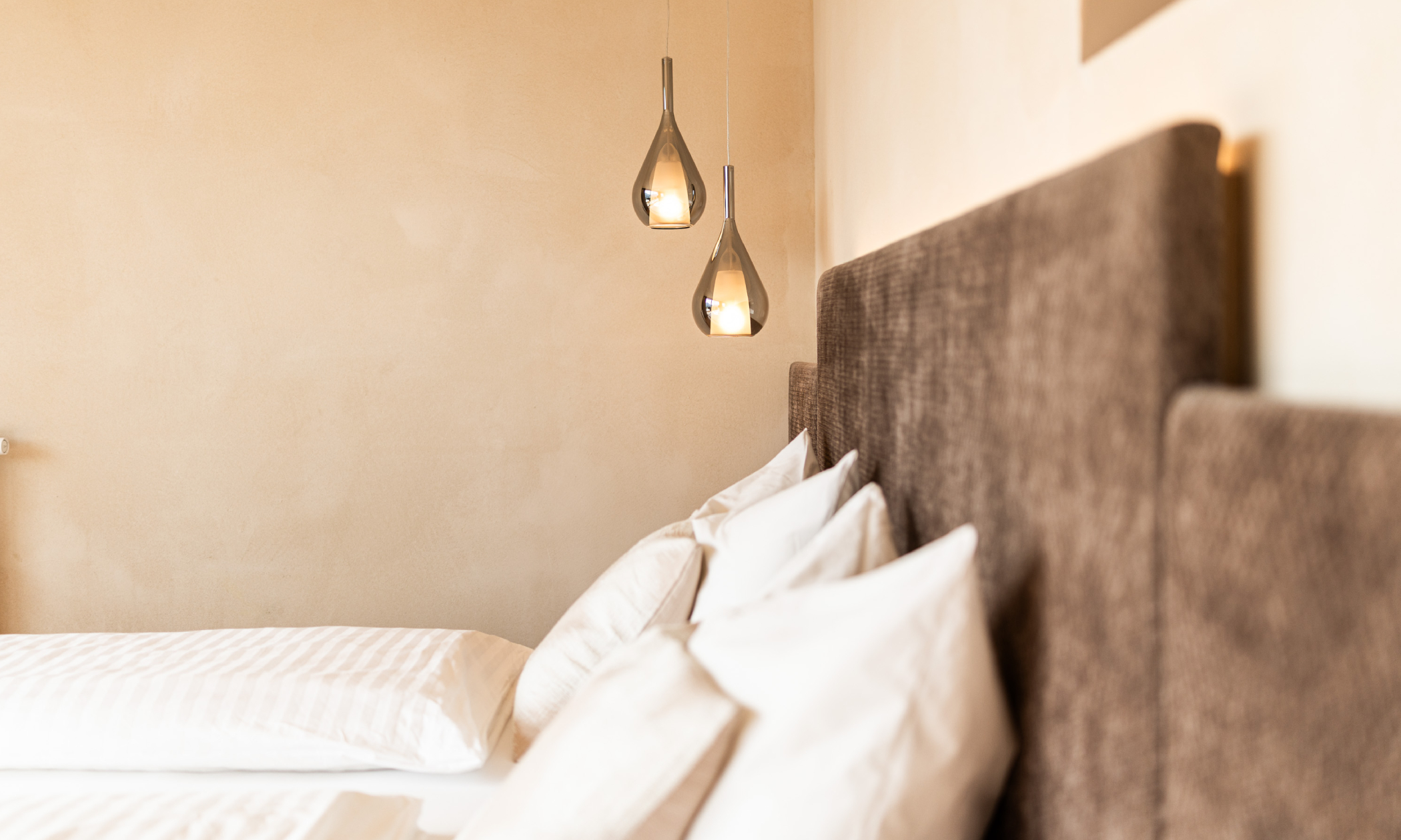 sauber gemachtes Bett mit modernen Hängelampen - Egger Apartments & Suites