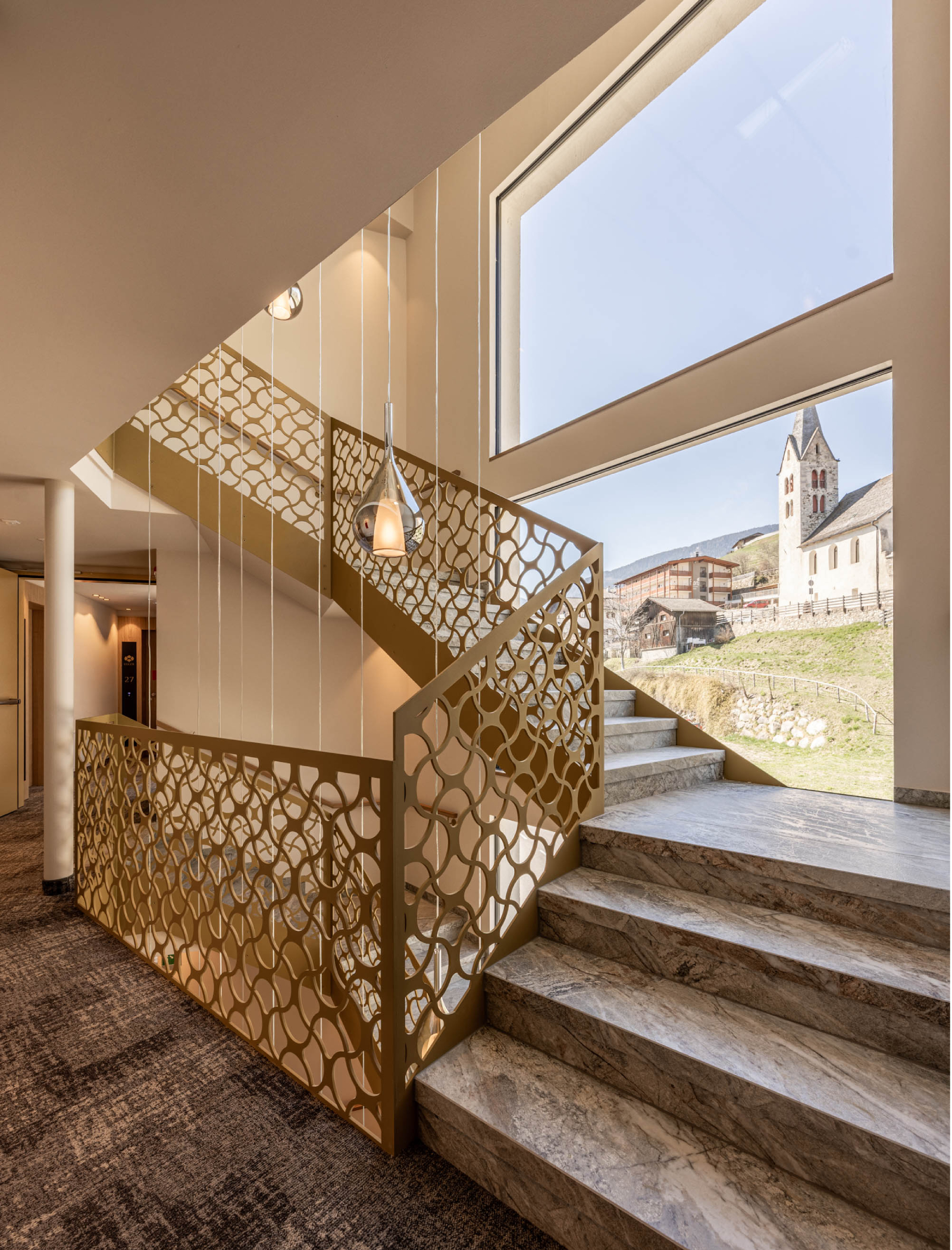 Stiegenhaus mit Geländer und modernen Hängelampen - Egger Apartments & Suites