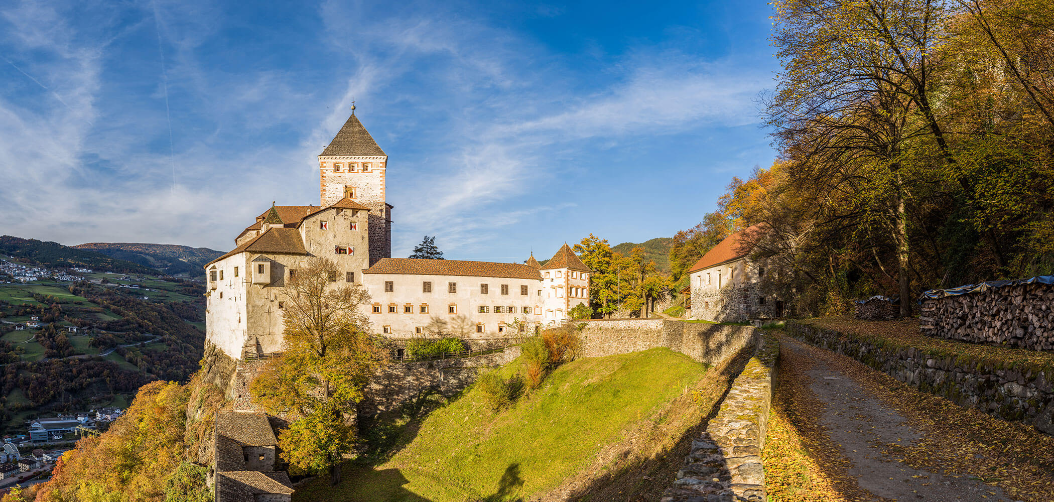 Mittelalterliche Burg auf einer Hügelkuppe, umgeben von Bäumen und einem Steinweg unter blauem Himmel. - Egger Apartments & Suites
