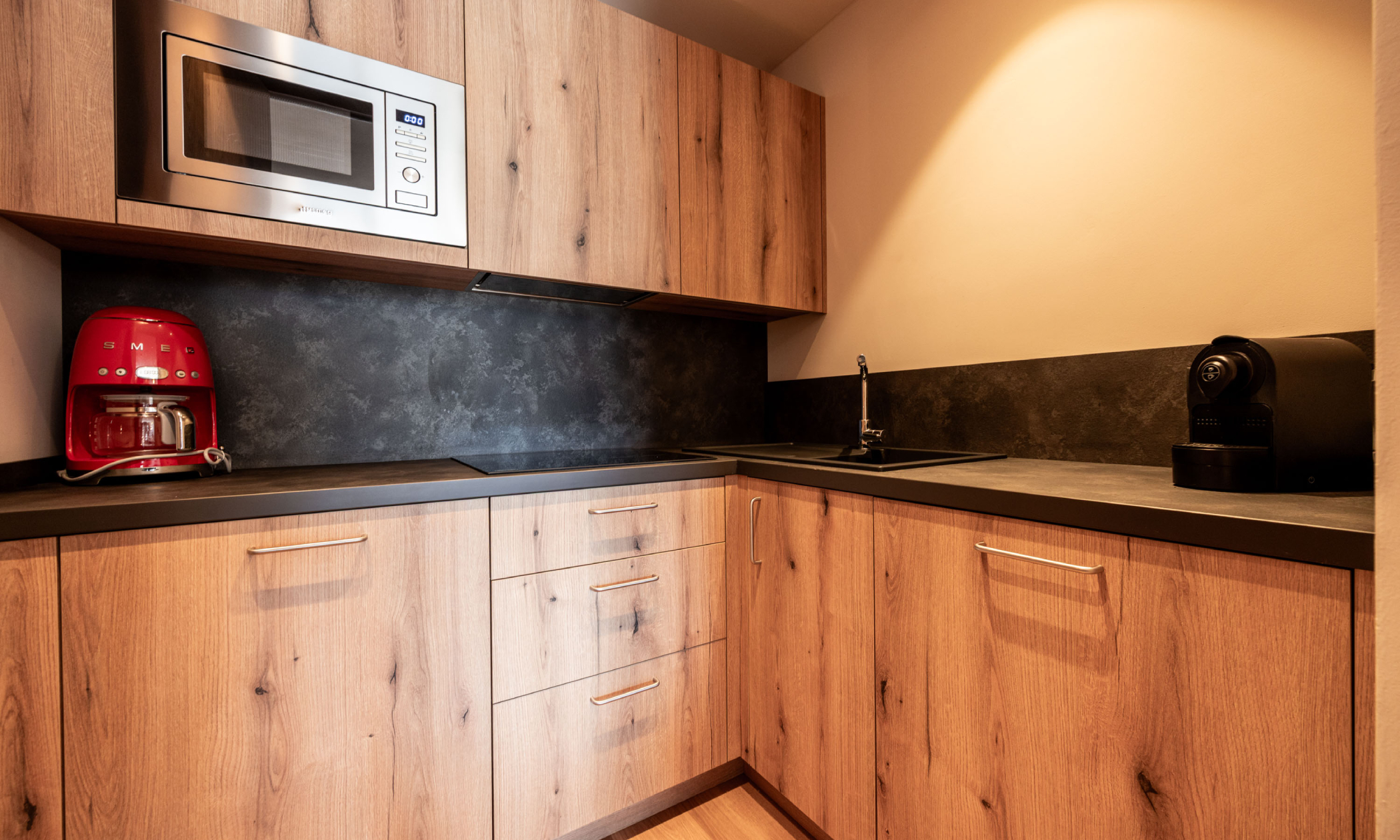 Küche aus Holz mit roter Kaffeemaschine, Espressomaschine und Tür zum schließen - Egger Apartments & Suites