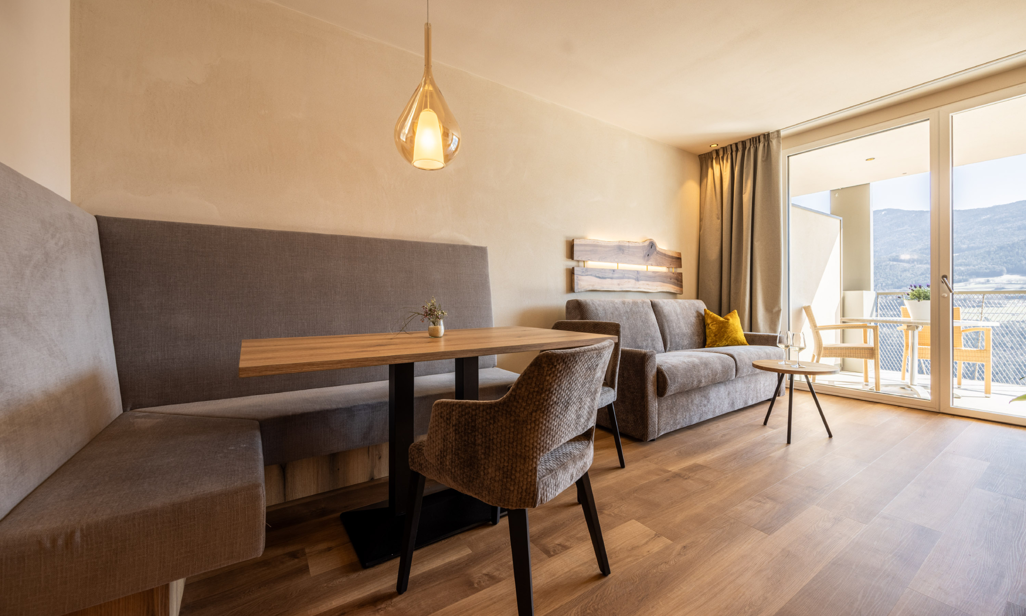 Wohnraum mit gemütlicher Sitzecke, brauner Couch, ockerfarbenen Kissen, großen Fenstern und weiter Panoramablick