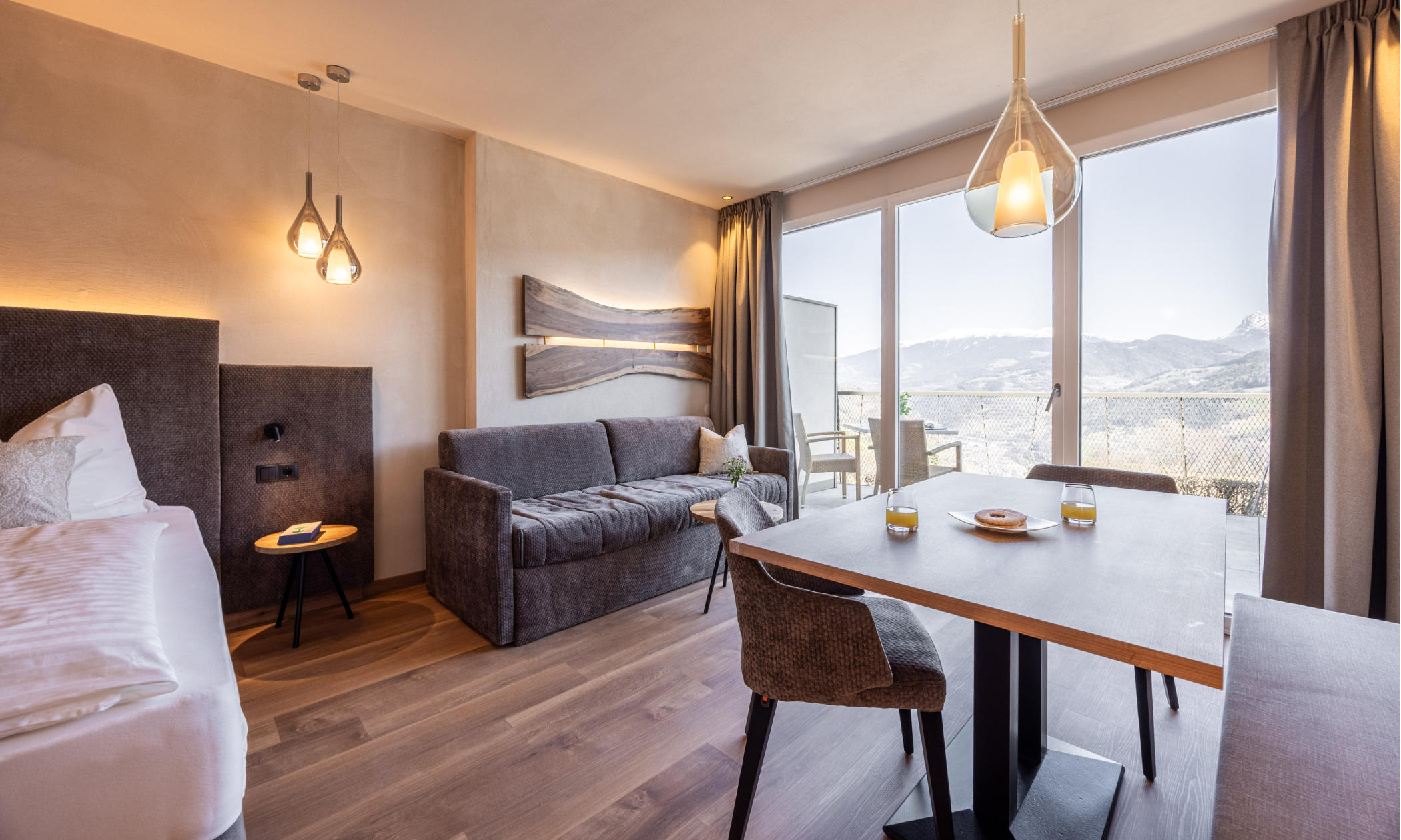 Tisch mit Stühlen, braune Couch und große Fenster mit Blick auf die Berge - Egger Apartments & Suites