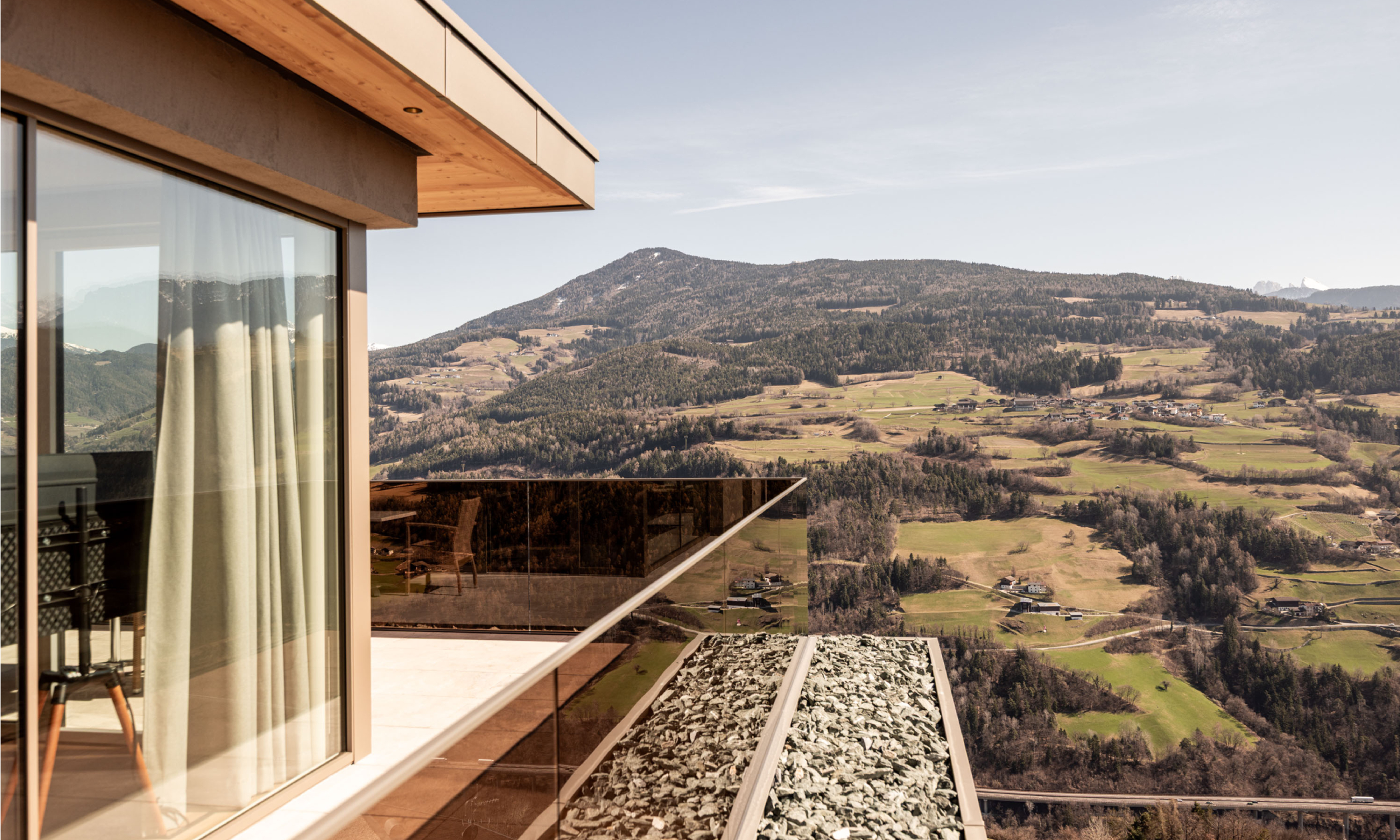 Terrasse mit Geländer aus Glas mit Ausblick ins Tal und auf die Dolomiten