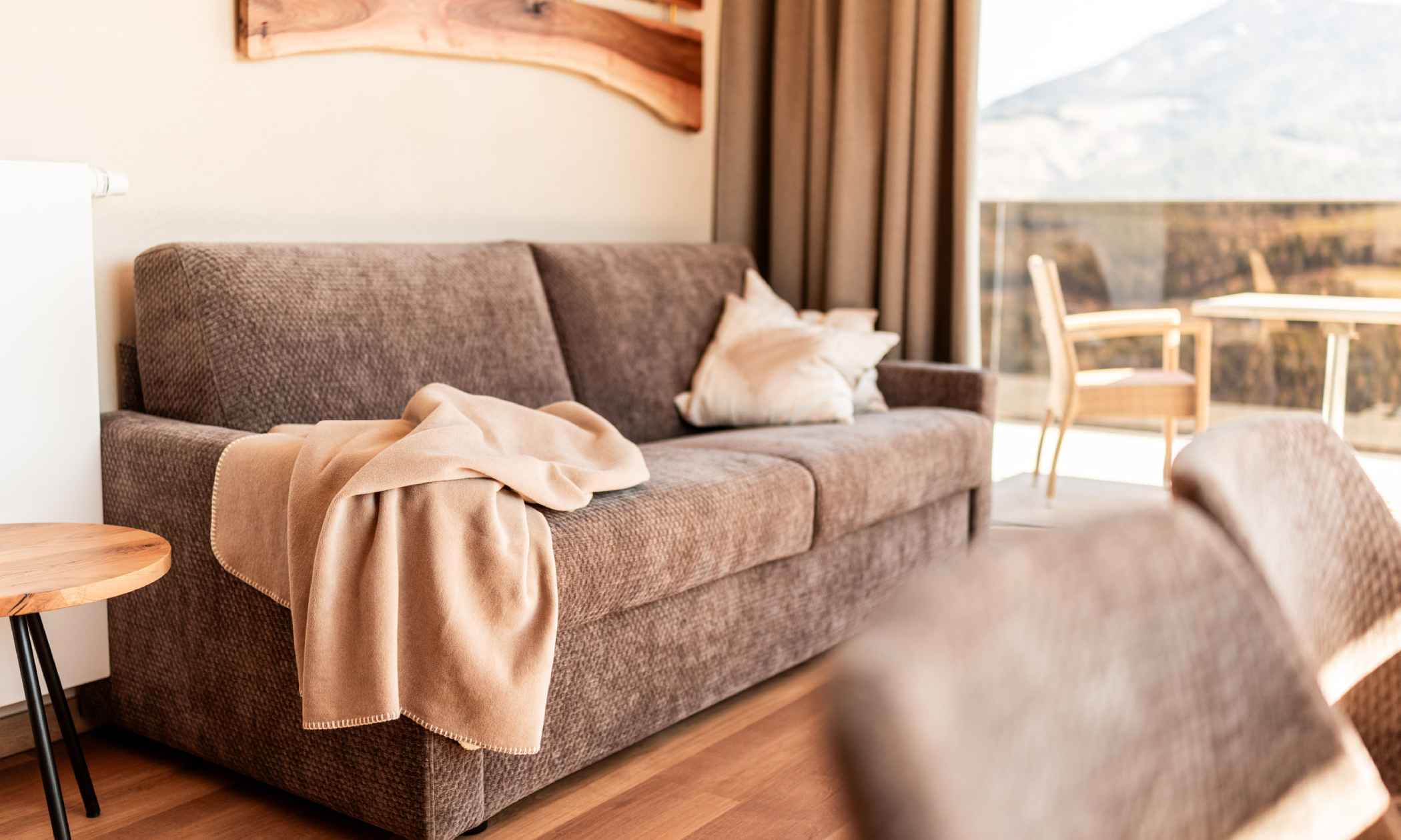 braune moderne Couch mit hellen Kissen und warmer kuscheliger Decke - Egger Apartments & Suites