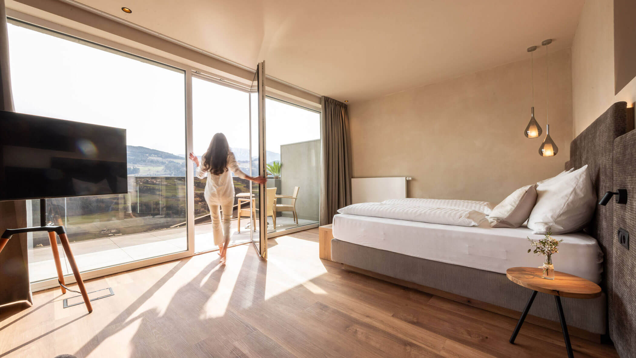 Modernes Schlafzimmer mit großem Bett, Balkon und Bergblick durch die Glastüren. – Egger Apartments & Suites