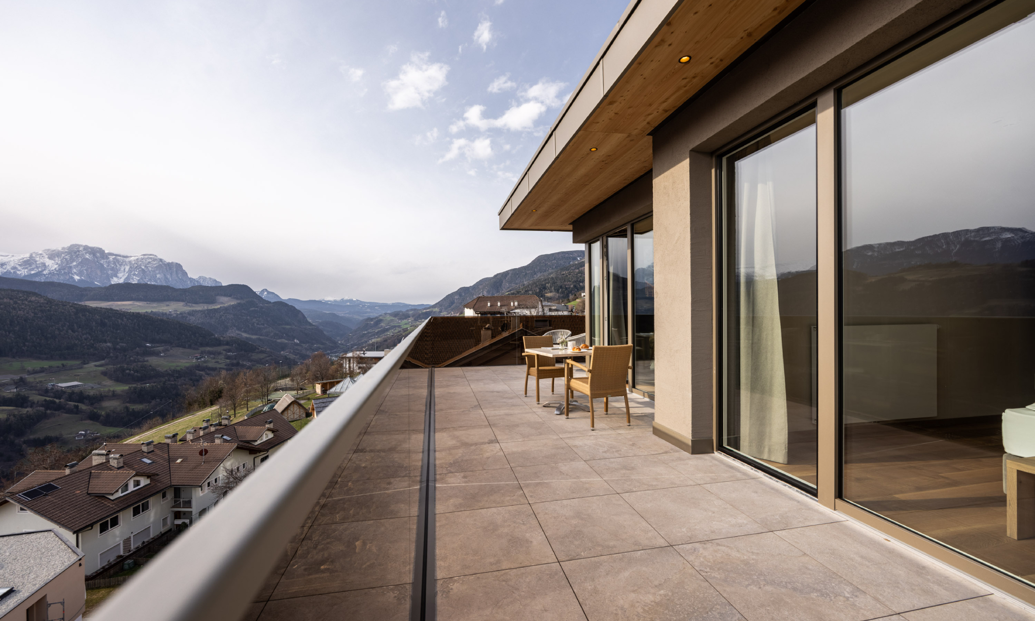 große Terrasse mit Tisch und Stühlen und Blick auf die Dolomiten und ins Tal - Egger Apartments & Suites