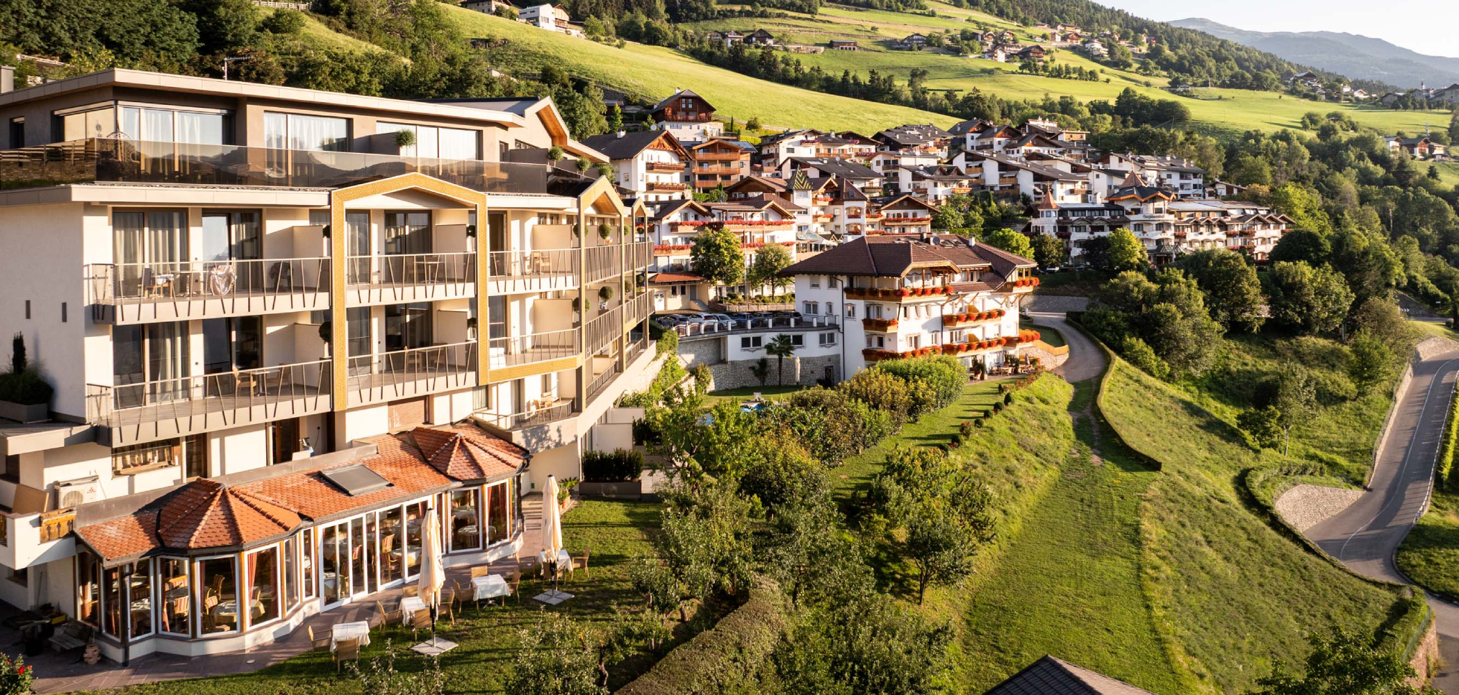 Moderno edificio a più piani con balconi situato su un pendio, circondato da case tradizionali - Egger Apartments & Suites