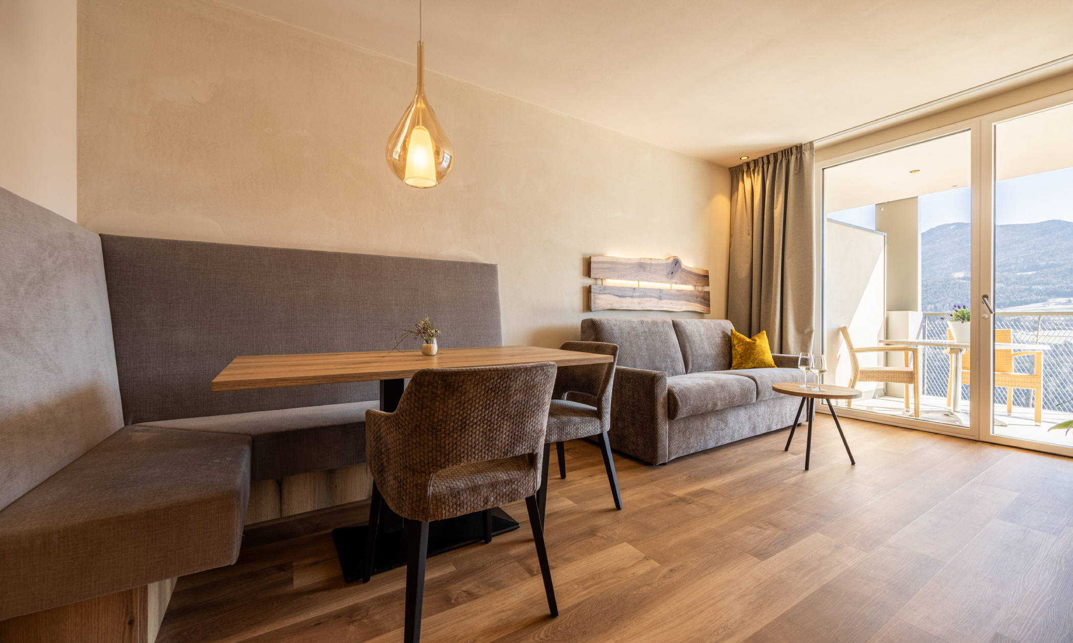 Wohnraum mit gemütlicher Sitzecke, brauner Couch, ockerfarbenen Kissen, großen Fenstern und weiter Panoramablick